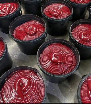 Multiple black containers filled with glossy red spiral-patterned desserts or sauces arranged on a metal surface