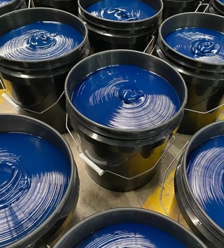 Multiple black buckets filled with vibrant blue paint arranged on a concrete floor